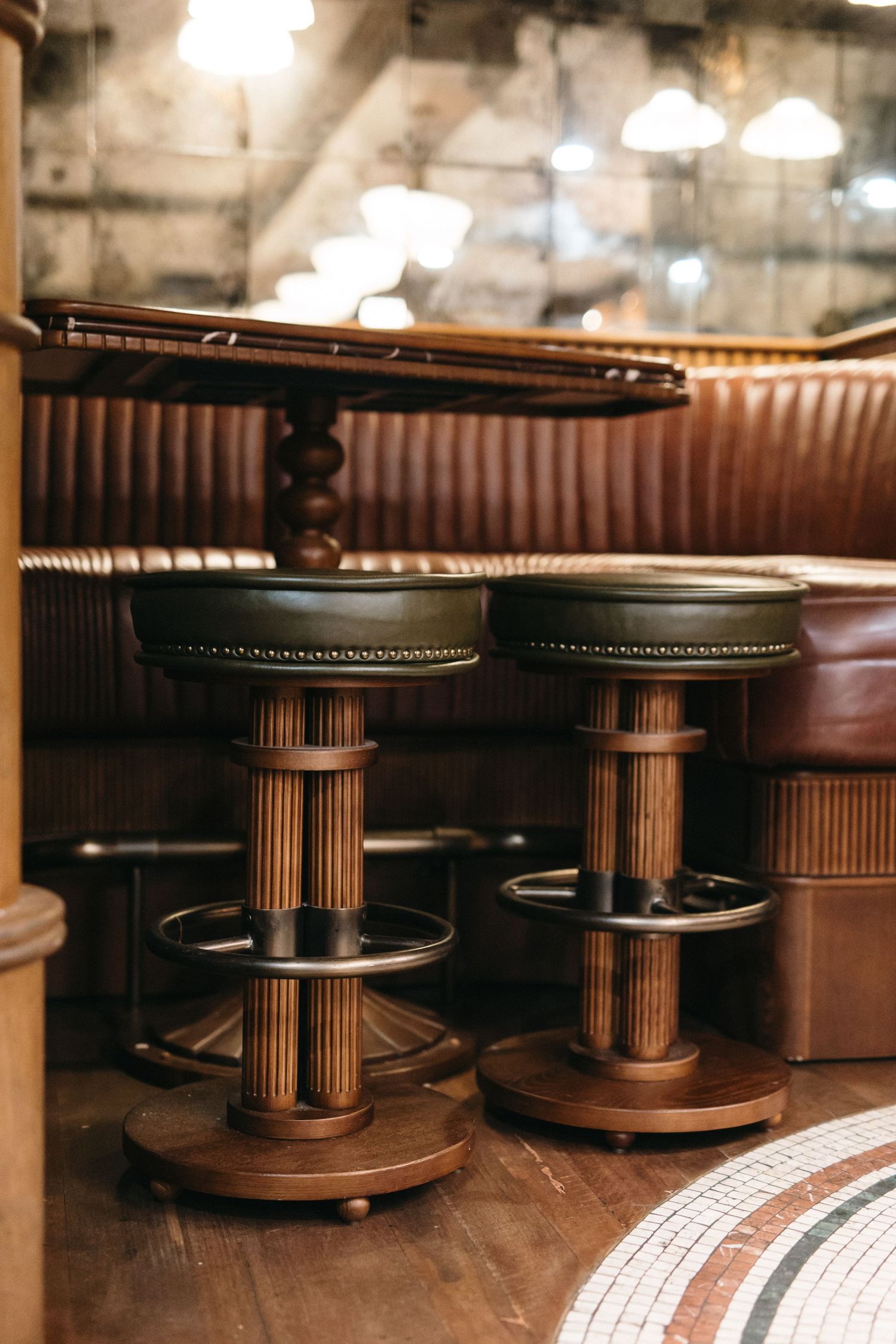 Vintage bar stools with wooden bases beside a brown leather booth in a warmly lit rustic restaurant interior.