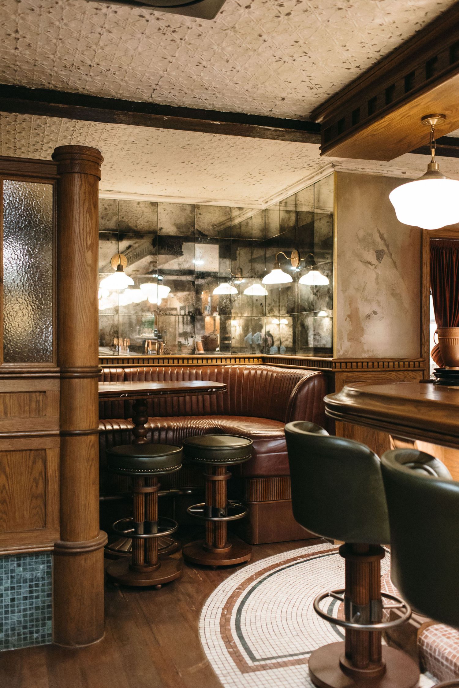 Vintage bar interior with leather booths, wooden columns, bar stools, and antique mirrored walls in a classic pub setting.