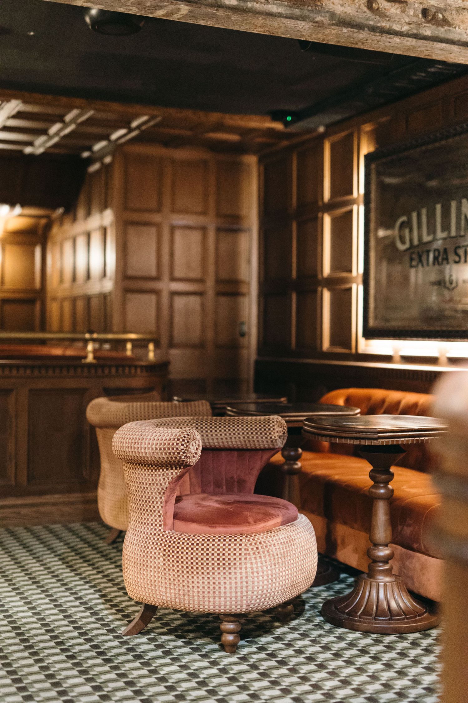 Vintage pub interior with pink velvet tufted chair, wooden paneling, and Gillies Extra Stout sign.