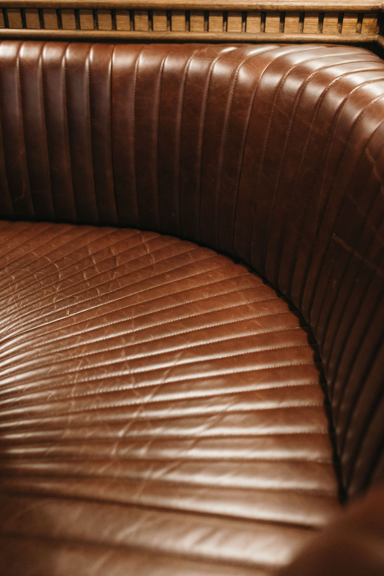 Close-up of a curved brown leather booth seat with vertical channel tufting in a vintage restaurant setting.