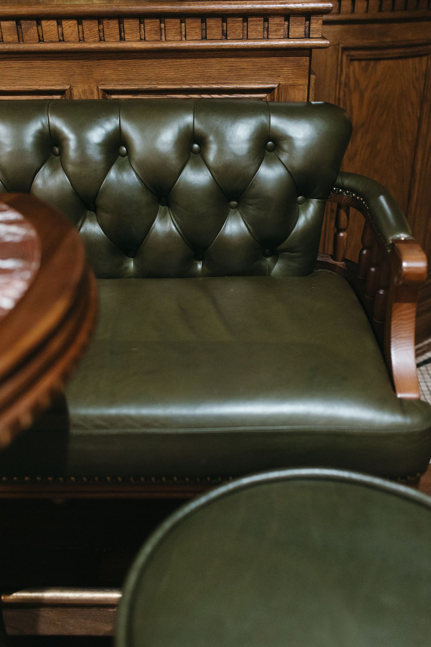 Elegant green tufted leather armchair with wooden frame in a classic interior setting.