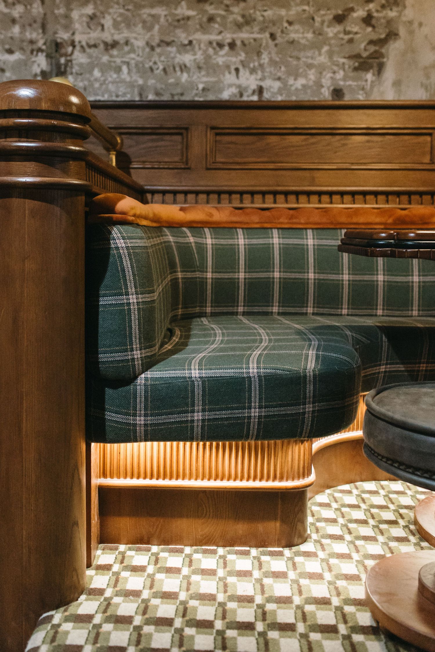 Green plaid upholstered booth seating with wooden trim and ribbed base in a cozy restaurant interior.