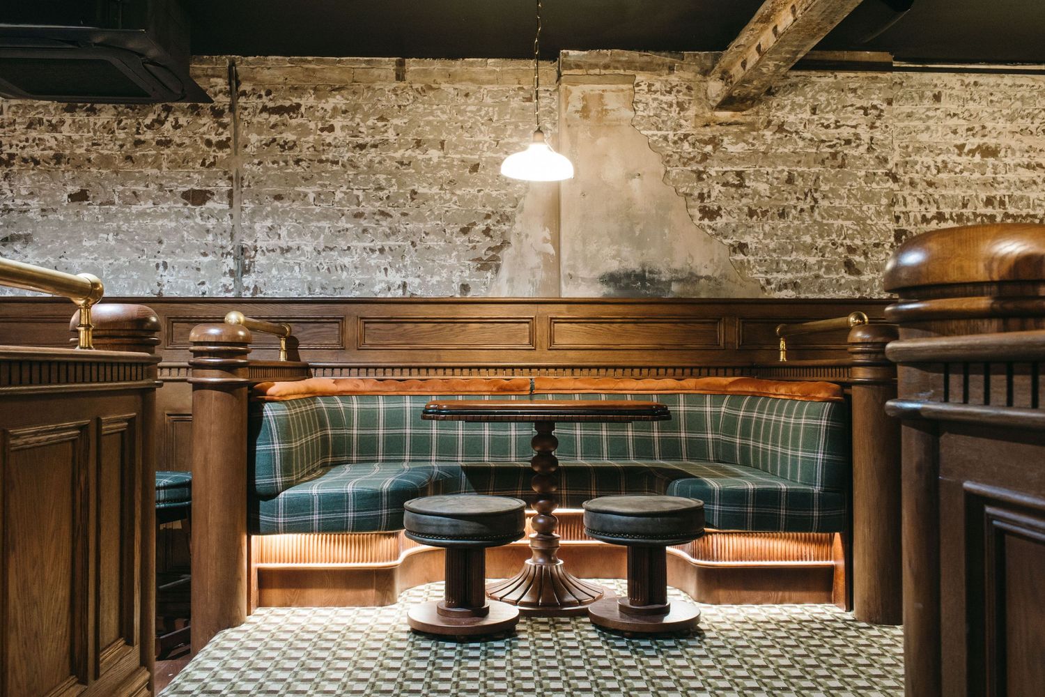 Cozy pub booth with plaid green velvet seating, ornate dark wood paneling, and vintage pendant light over mosaic tile floor.