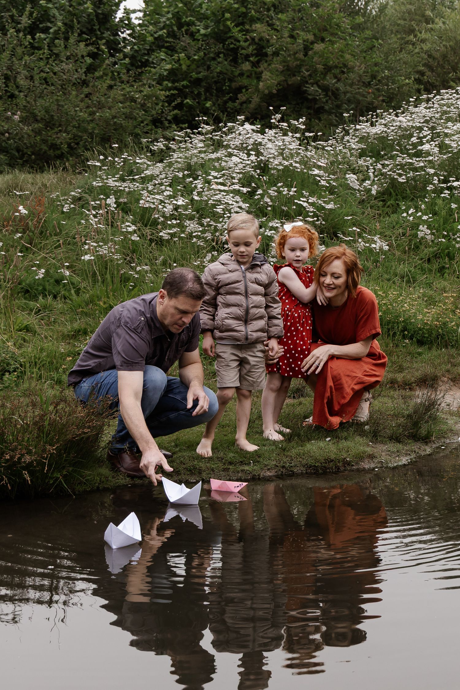 Kids playing with their parents and floating paper boats in the water during a family photoshoot in Woerden