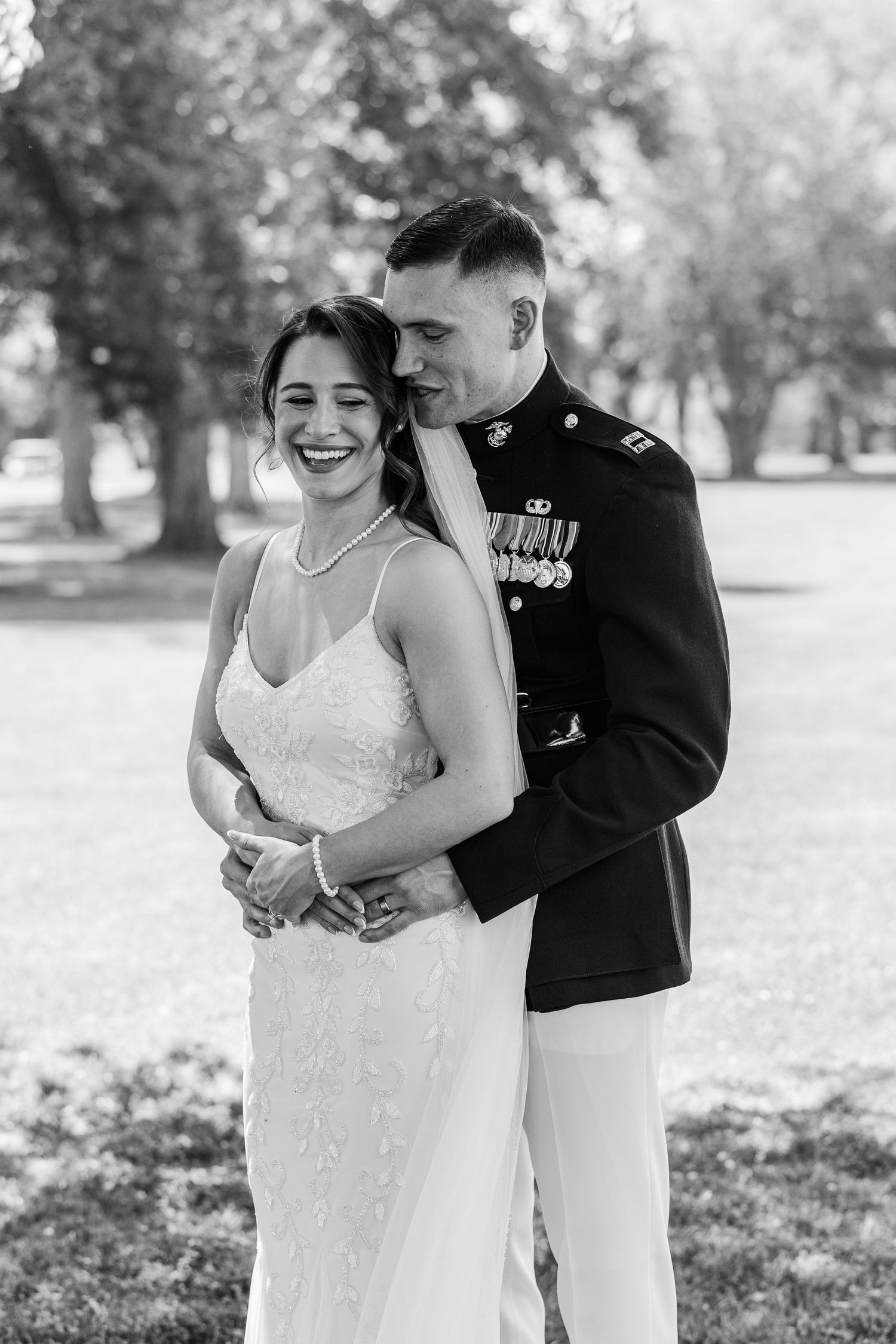 Black and white photo of a bride and groom sharing a kiss under a flowing veil outdoors.