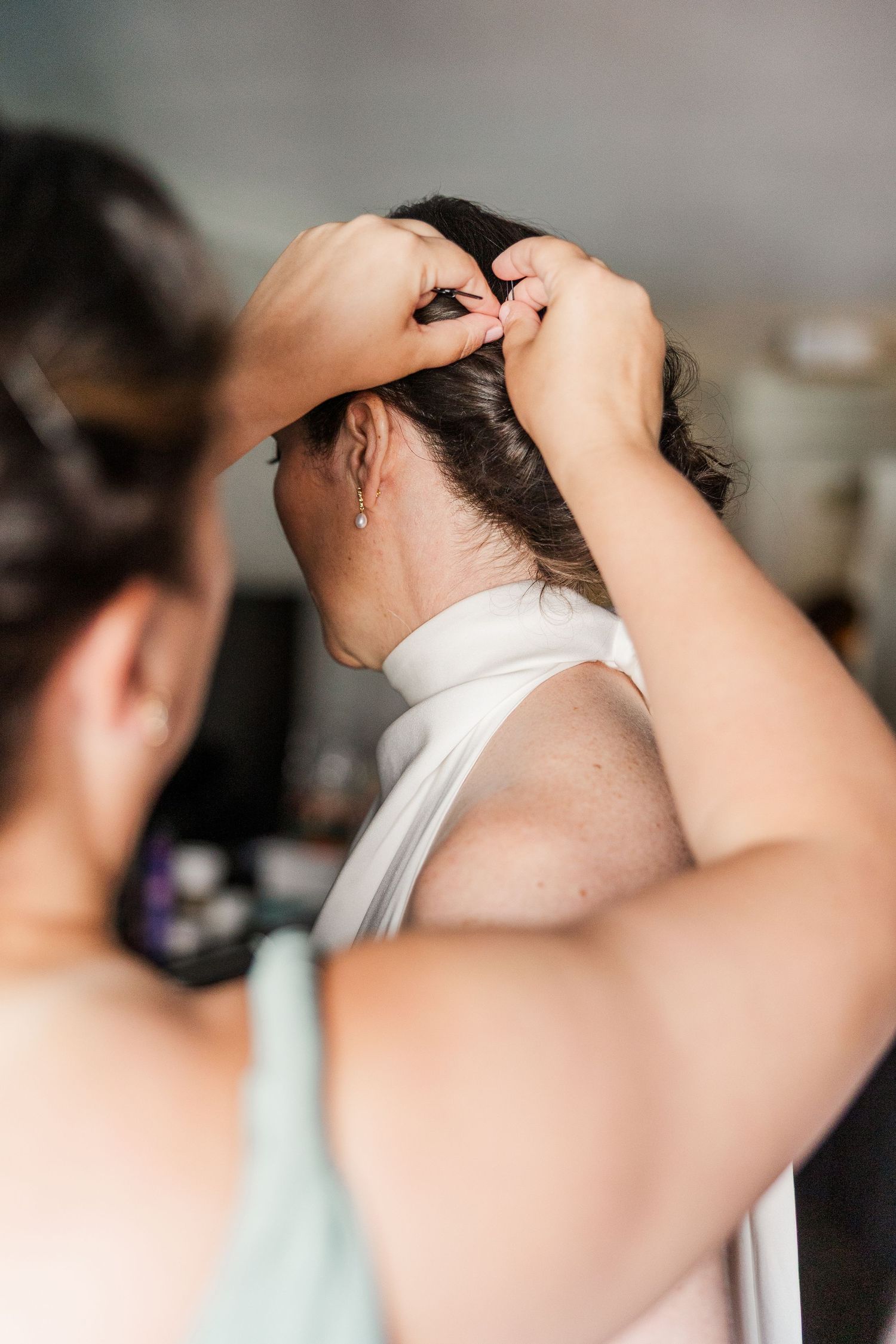 Bridesmaid helping bride with hair styling, pinning up dark updo hairstyle before wedding ceremony.