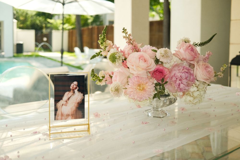Elegant wedding table with pink peony floral arrangement in crystal vase and framed photo beside an outdoor pool.