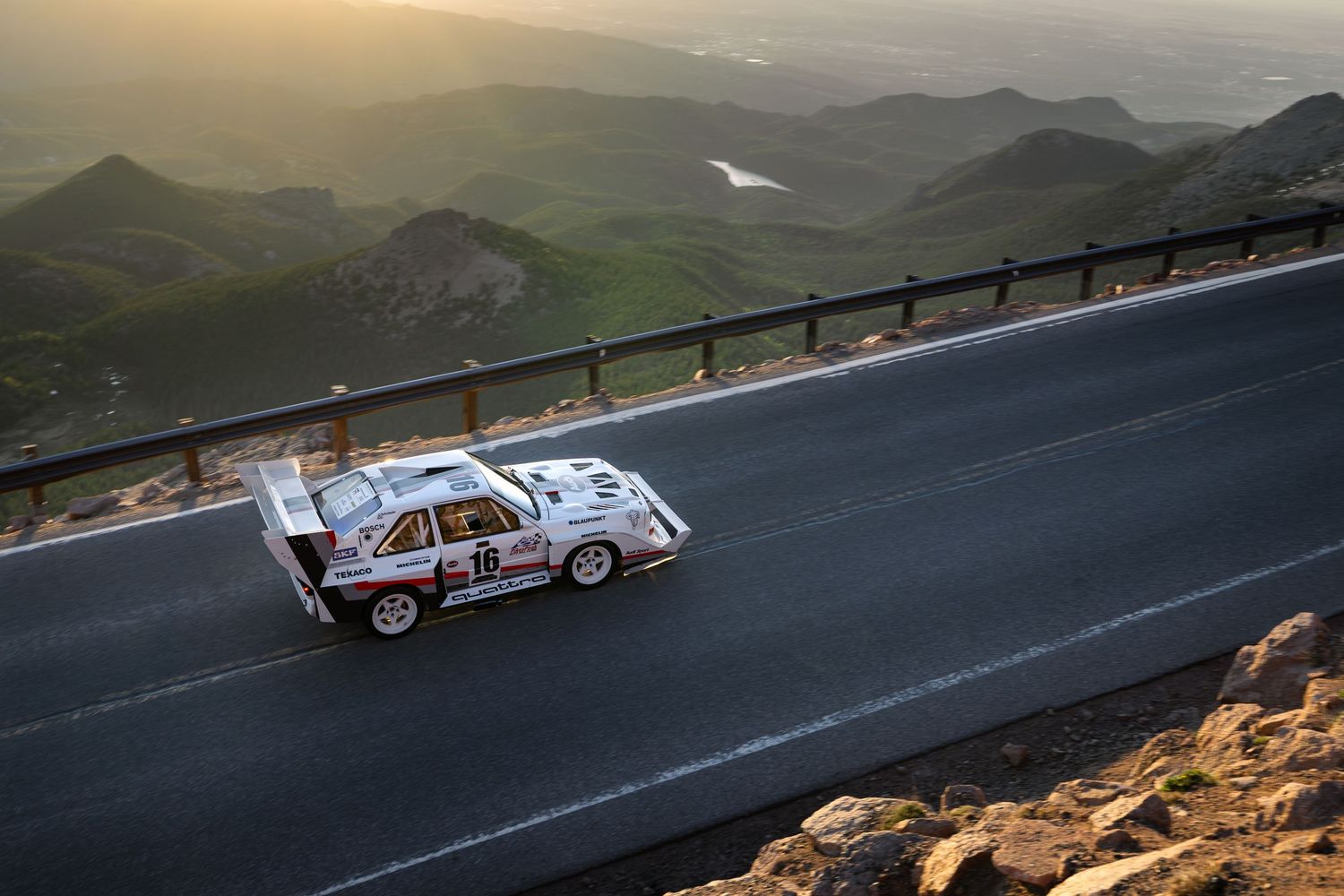 Vintage Porsche 550 Spyder racing on snow-covered alpine track with dramatic mountain backdrop in winter.