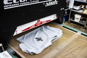 Gray t-shirts being cured under an infrared curing system machine in a screen printing facility.