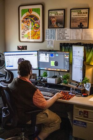 Person working at a dual-monitor desk setup with Muppets posters on the wall in a creative office workspace.