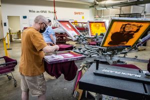 Worker operating a screen printing press machine in a professional print shop facility.