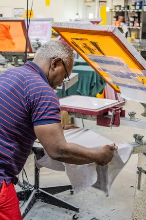 Man in striped shirt operating screen printing equipment in a professional print shop.