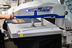 Air Fusion heat press machine in operation at a garment printing facility with a dark shirt on the platen.