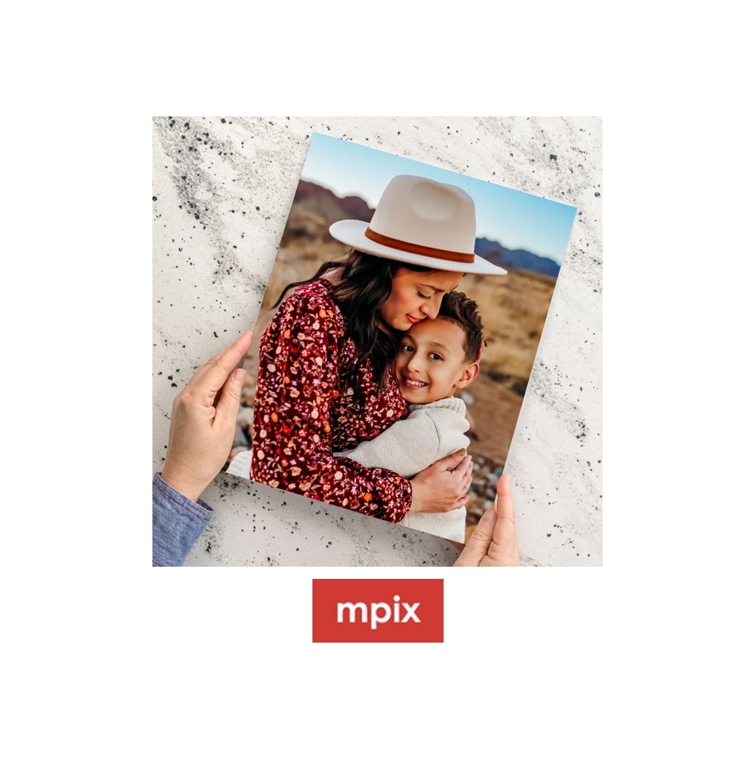 Hands holding an Mpix printed photo of a mother and child embracing outdoors, displayed on a marble surface.