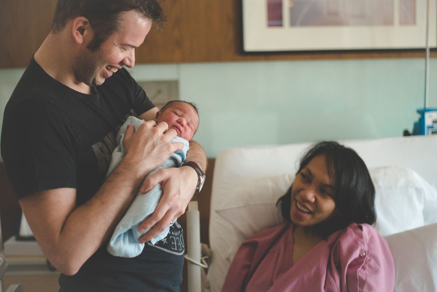New parents smiling at their newborn baby in a hospital room after birth.
