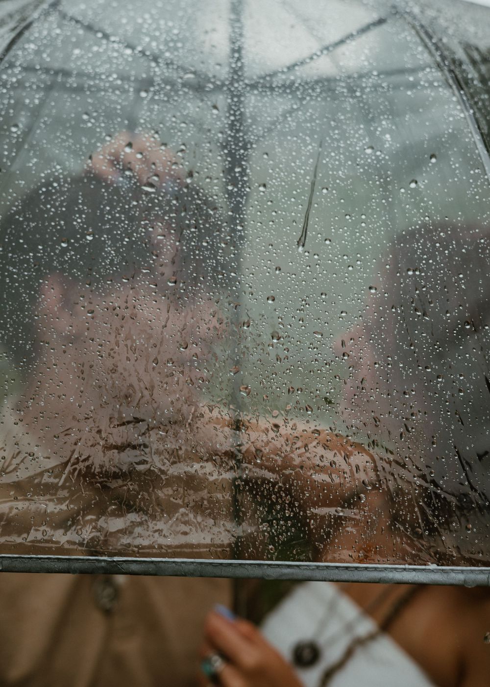 Artistic shot of couple kissing behind a rain-covered clear umbrella in the rain.