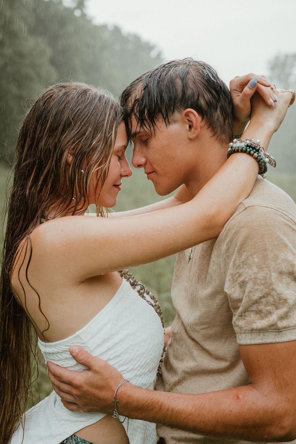 Young couple embracing intimately in the rain, foreheads touching romantically in a misty outdoor setting.
