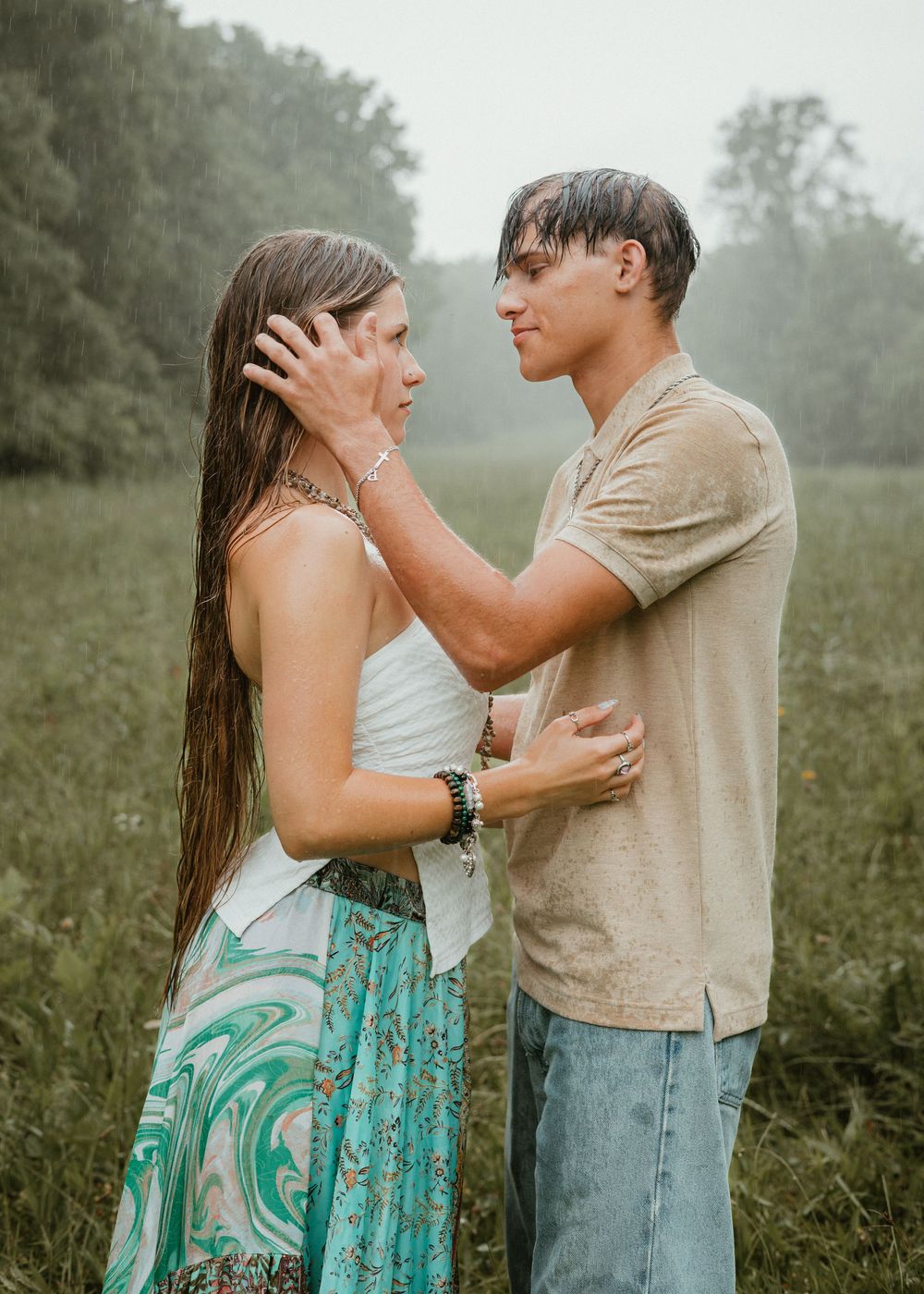 Romantic couple standing in a rainy meadow, man gently touching womans face while gazing into her eyes.