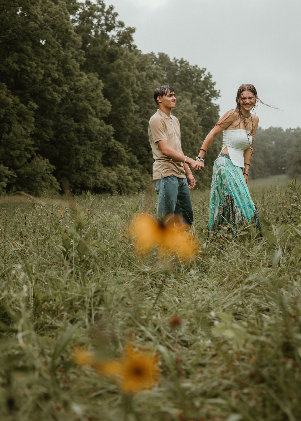 Young couple holding hands while walking through a wildflower meadow on a cloudy day.