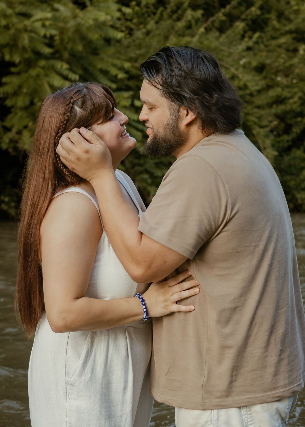 Couple sharing a tender moment near a creek, man cupping womans face as they smile together.