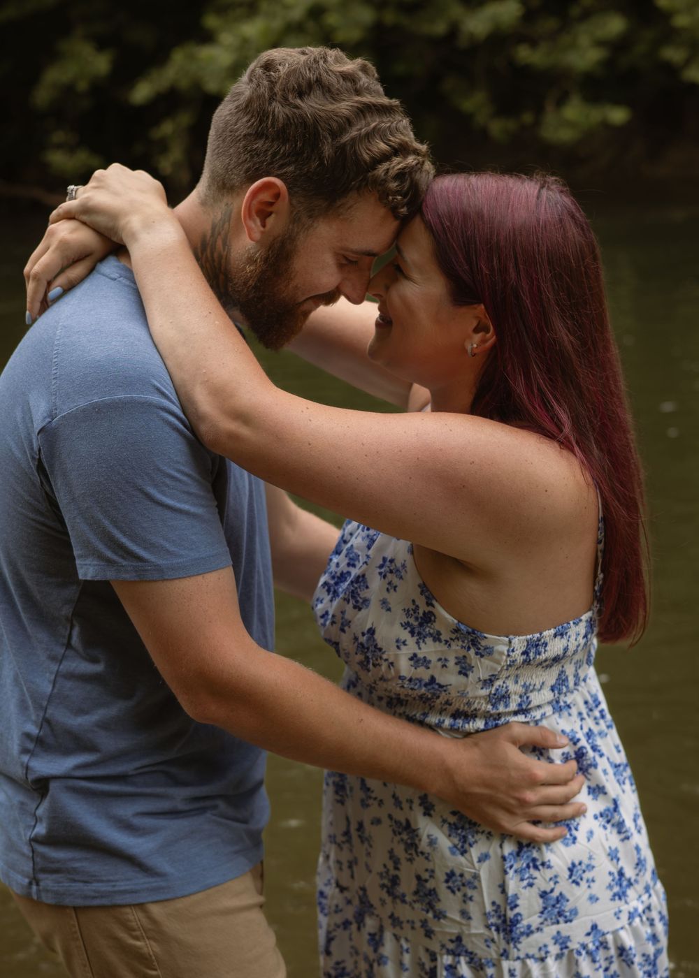Loving couple with foreheads touching, embracing near a forest creek in a tender romantic moment.