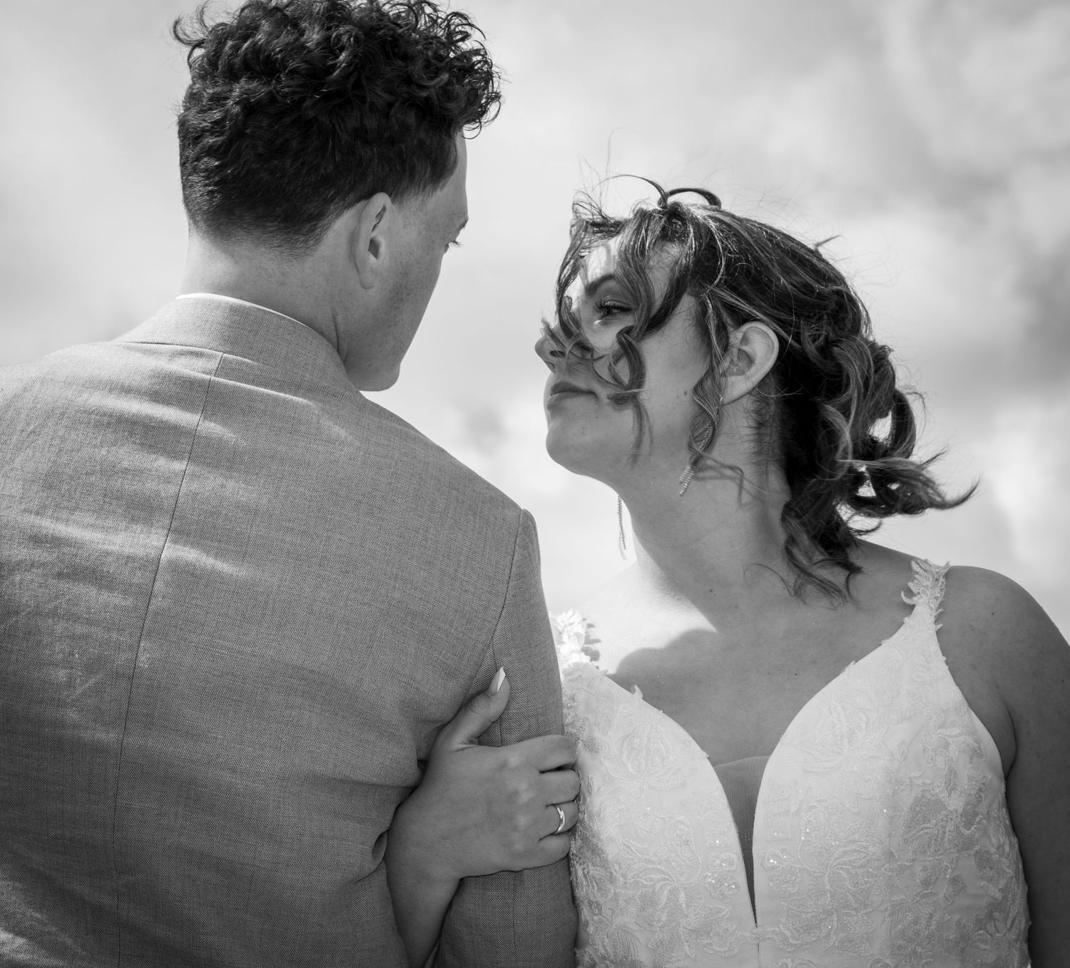 Black and white photo of bride smiling up at groom while embracing outdoors on their wedding day.