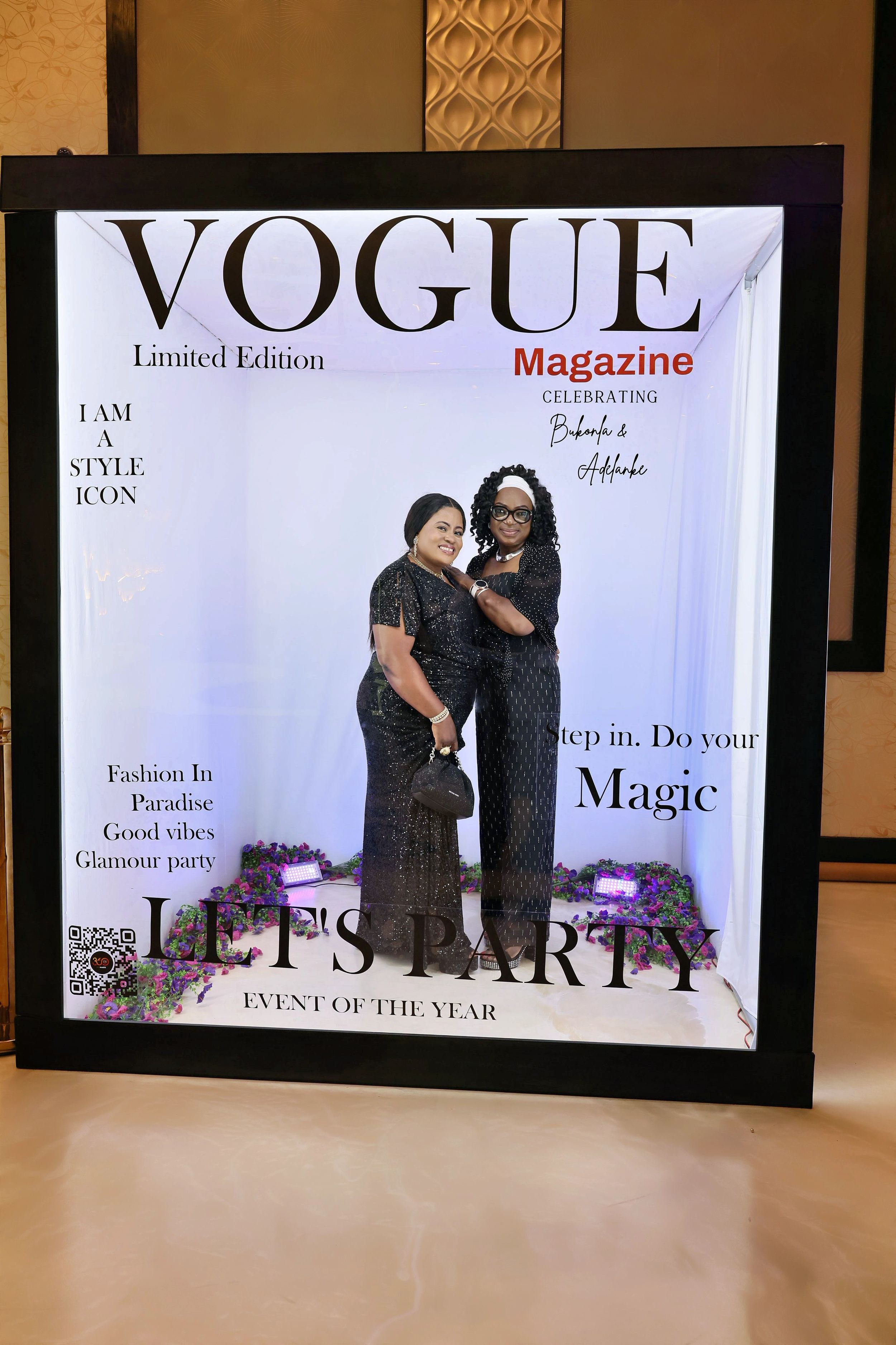 Two women in black outfits embracing inside a Vogue Magazine Limited Edition party photo booth.