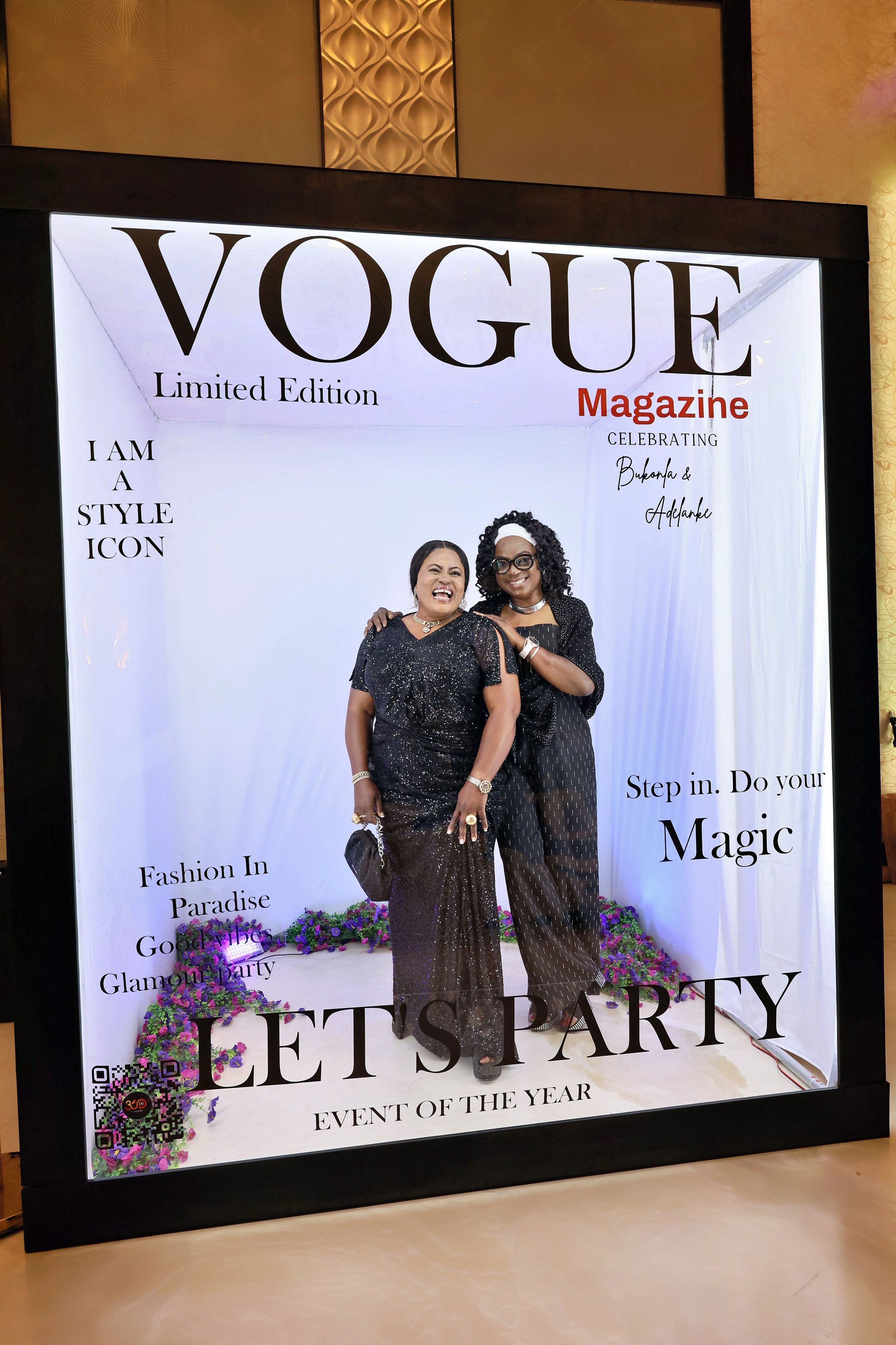 Two women in black dresses smiling inside a Vogue Magazine Limited Edition Let's Party photo booth.