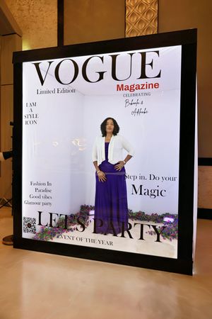 Woman in purple dress and white blazer at Vogue Magazine Lets Party photo booth.