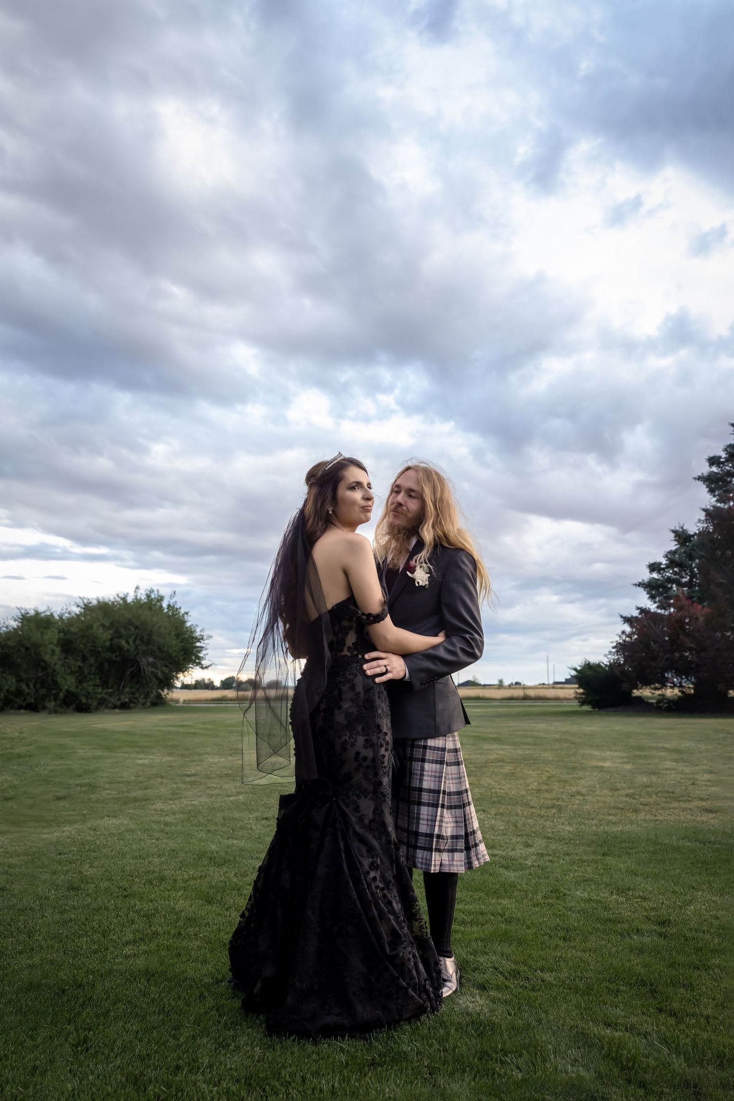 Castle Gardens Kuna Idaho ©Milestones Studios LLC low angle portrait of bride in black and groom in kilt with dramatic cloudy sky