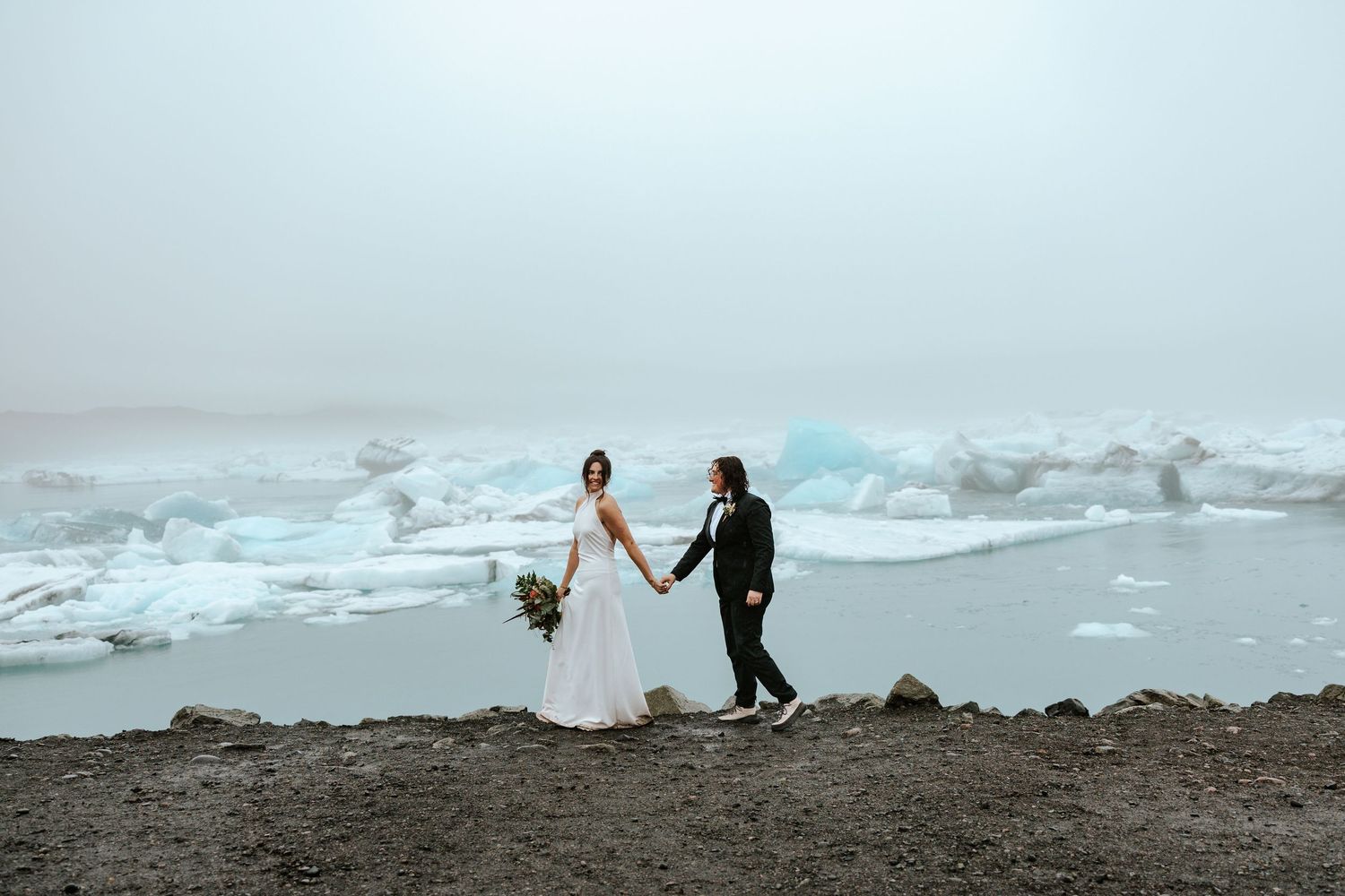 two brides walking along the edge of Jokulsarlon glacier lagoon in iceland during elopement day