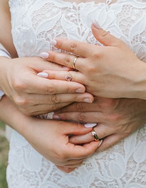 Couple embracing in wedding attire, showcasing gold wedding bands and a pink gemstone engagement ring.