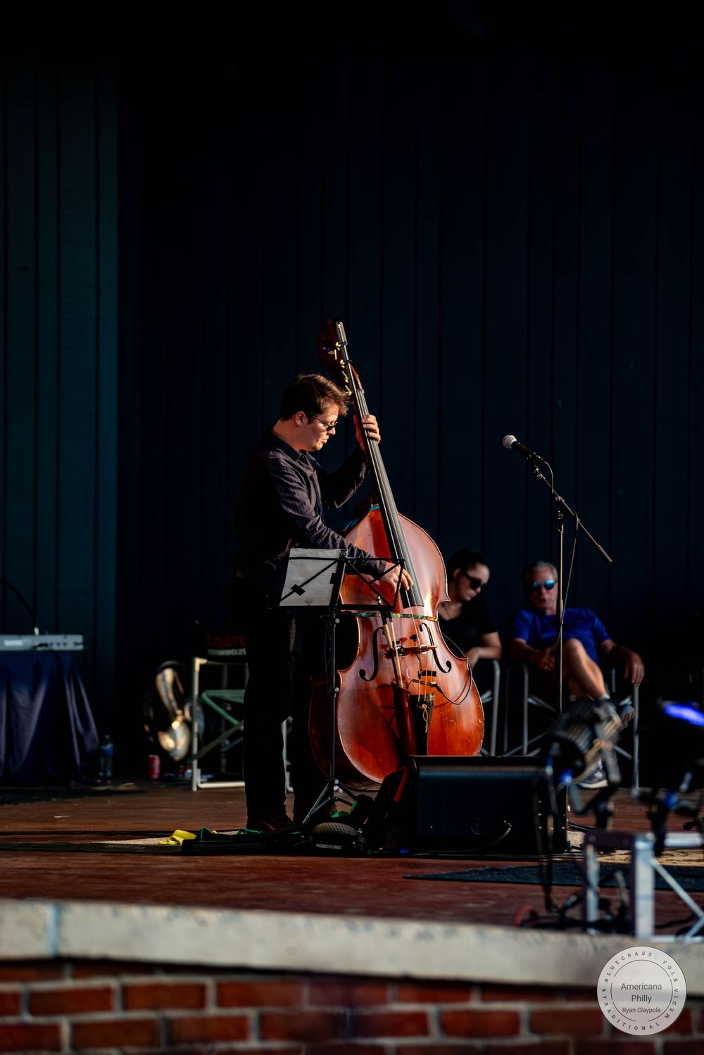 Musician playing upright double bass on outdoor stage at live jazz concert performance.