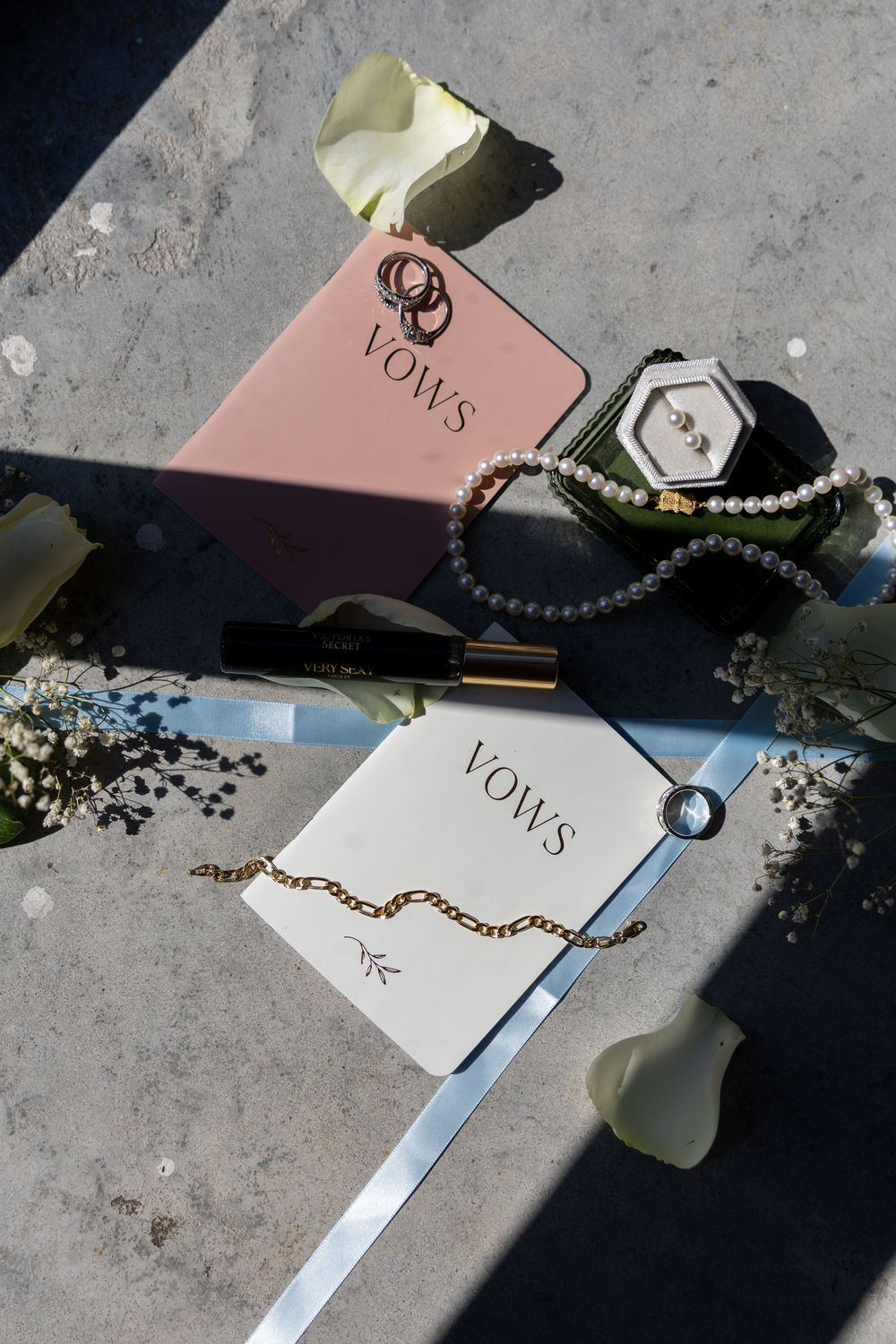Wedding vows books, pearl necklace, gold chain bracelet, ring box, and mirror on concrete surface.