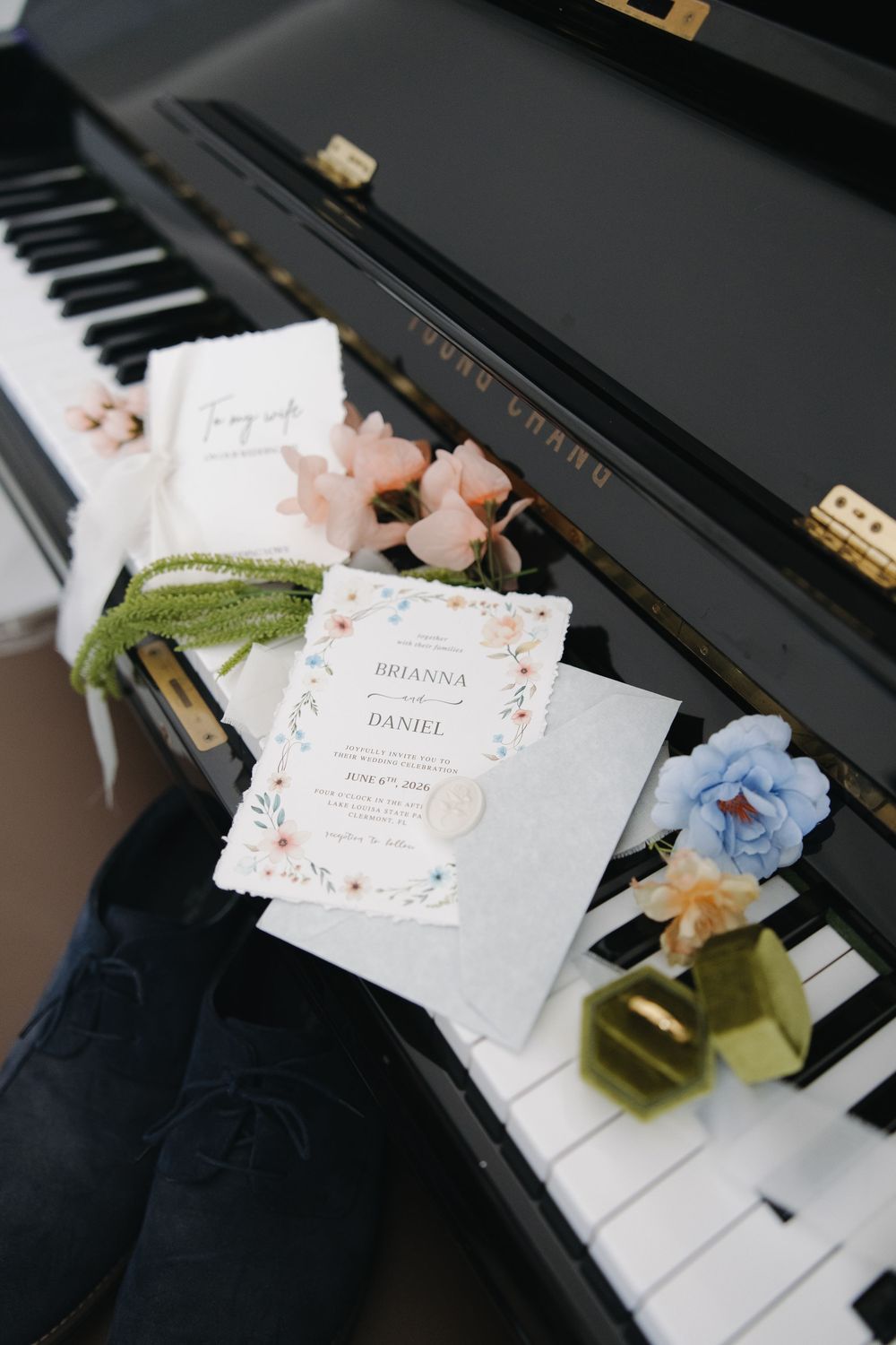 Wedding invitation suite for Brianna and Daniel displayed on piano keys with floral decor and velvet ribbon accents.