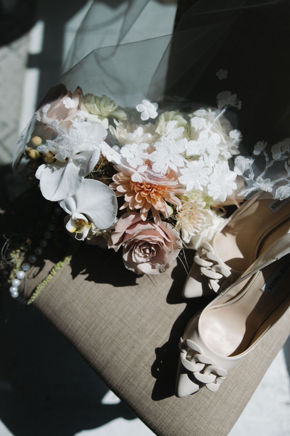 Bridal bouquet with blush roses and white flowers beside nude heels on a neutral surface.