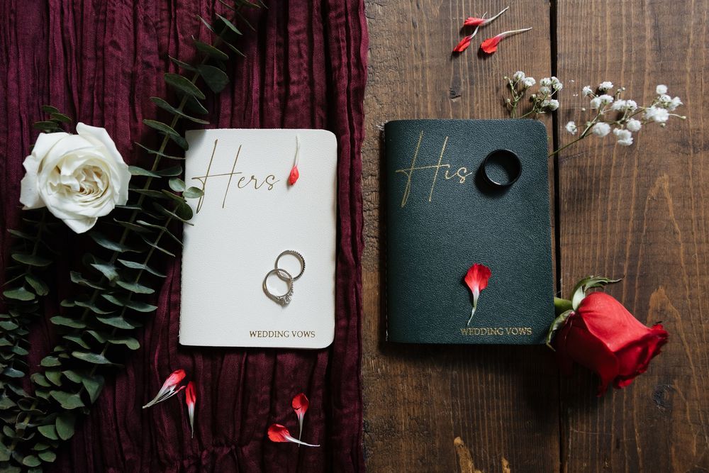 His and Hers wedding vow books with rings, white and red roses on wooden background.
