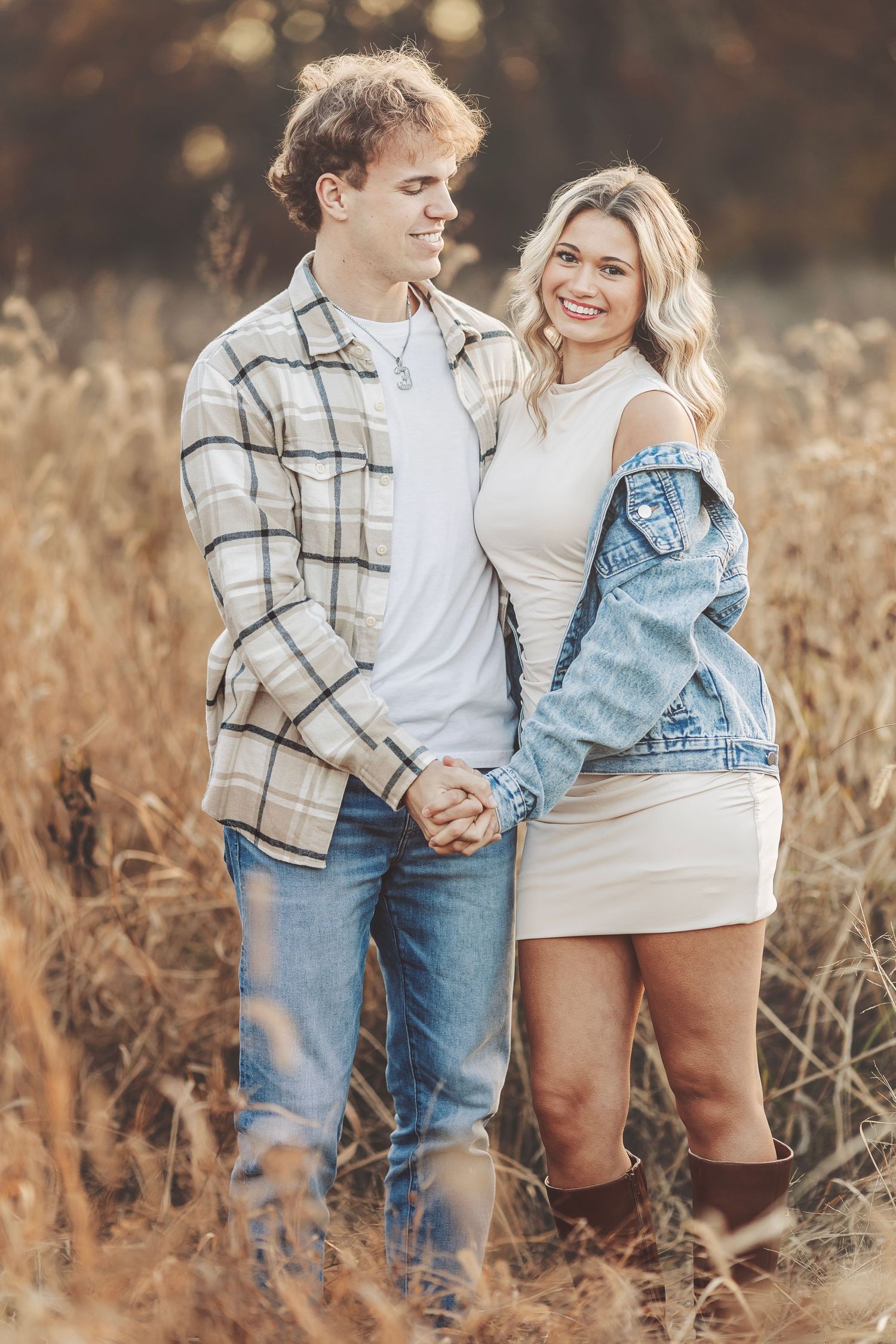 A couple shares a romantic kiss outdoors in warm golden autumn sunlight, surrounded by glowing fall foliage.