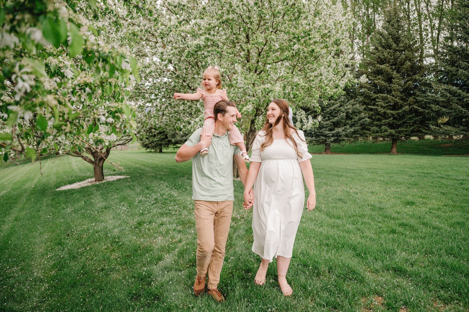 A family walking together on a sunny spring day in a lush green garden with blooming trees in the background.