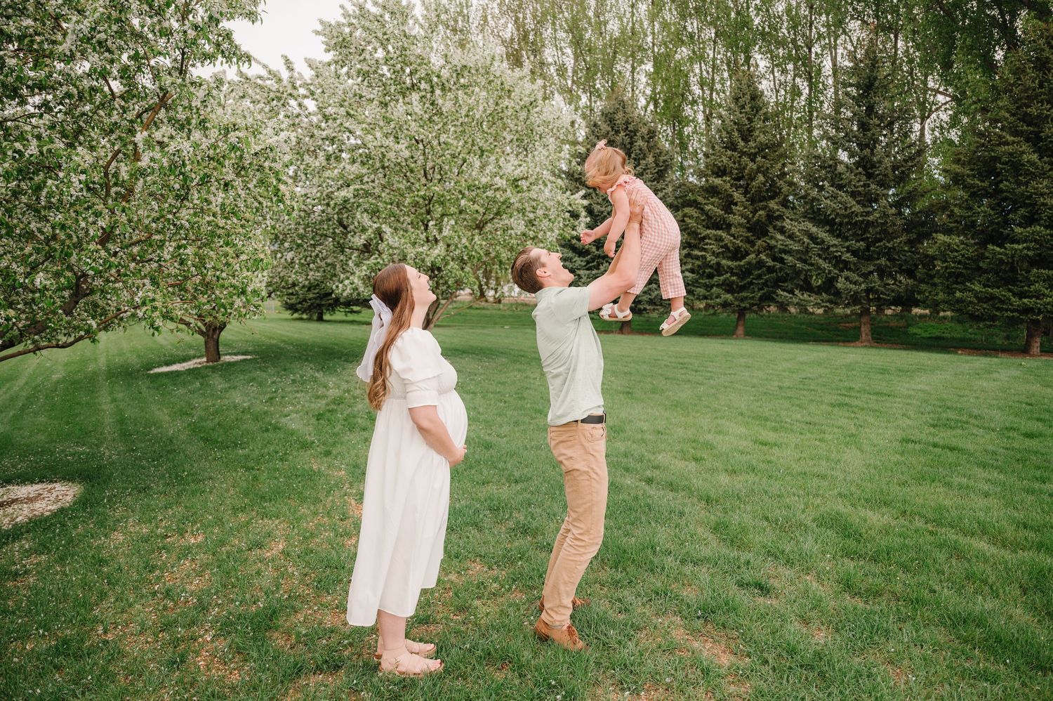 People enjoy a playful moment together on a lush green lawn surrounded by trees and bushes in a backyard setting.