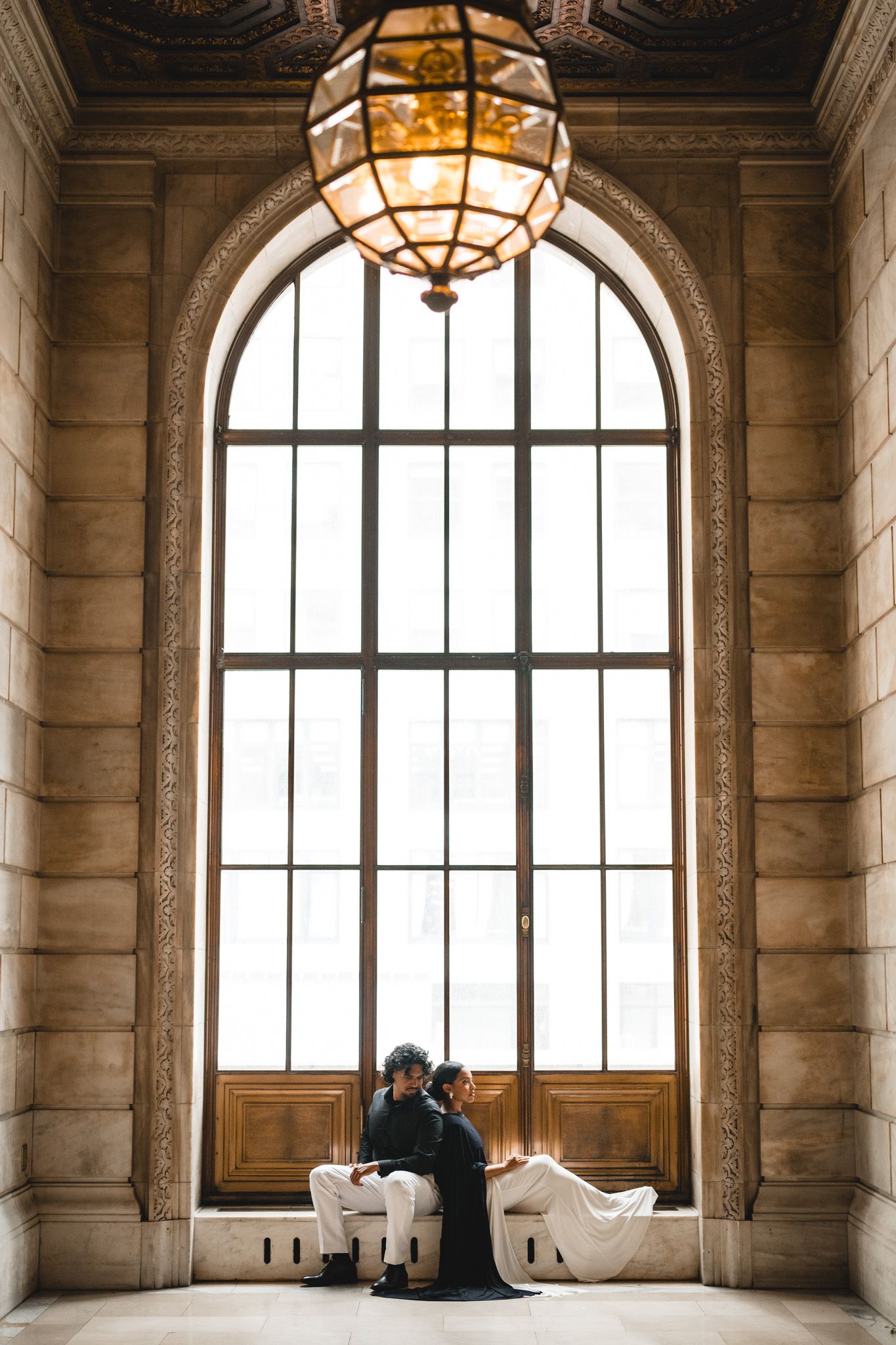 Romantic couple sitting together in a grand arched window alcove with ornate chandelier.