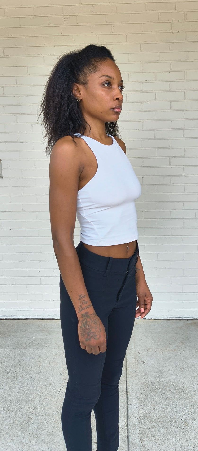Side (right) profile digital of Genesis Dudley wearing a white tank top and black pants.
