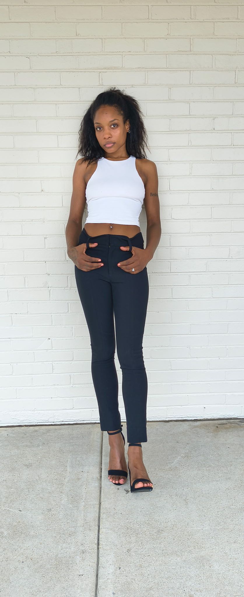 Full-length front digital of Genesis Dudley wearing a white tank top and black pants.