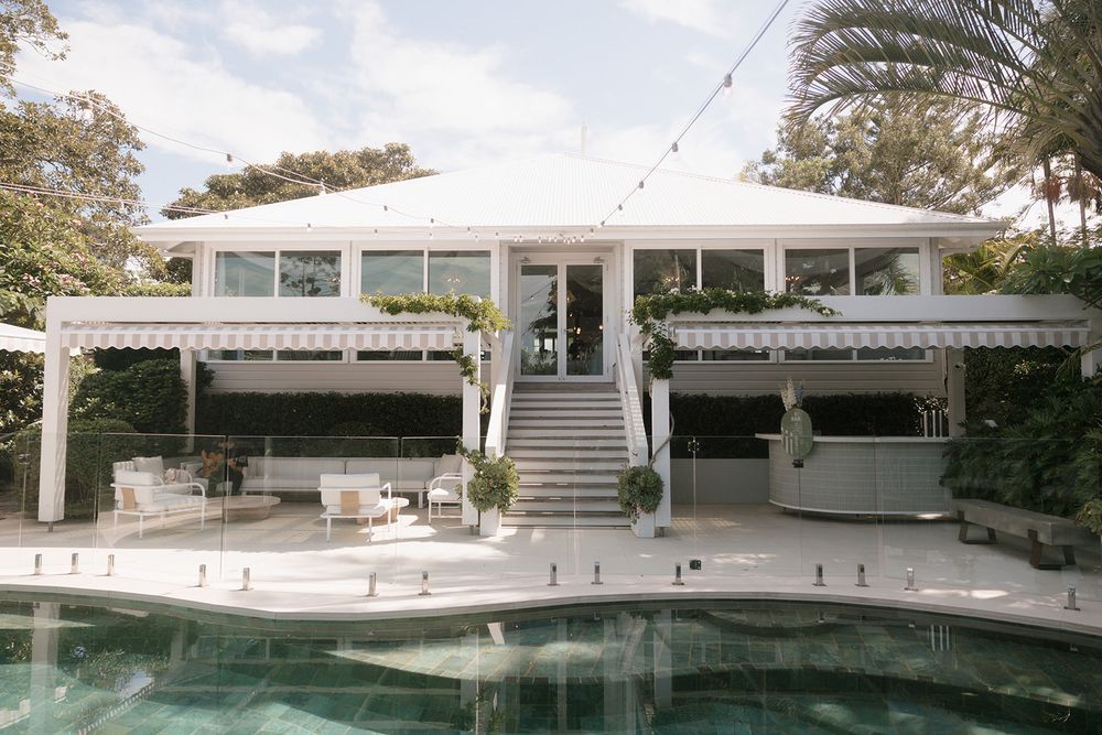 Elegant white poolside villa with pergola, glass railings, and lush tropical surroundings on a sunny day.