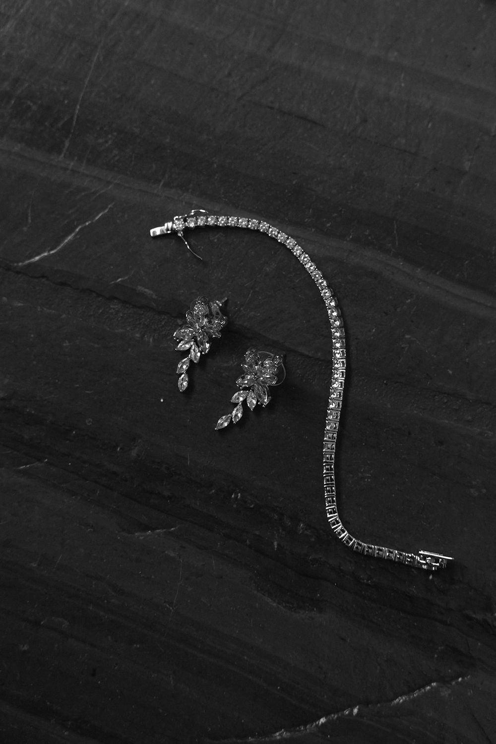 Elegant diamond tennis bracelet and floral cluster earrings displayed on dark marble surface.