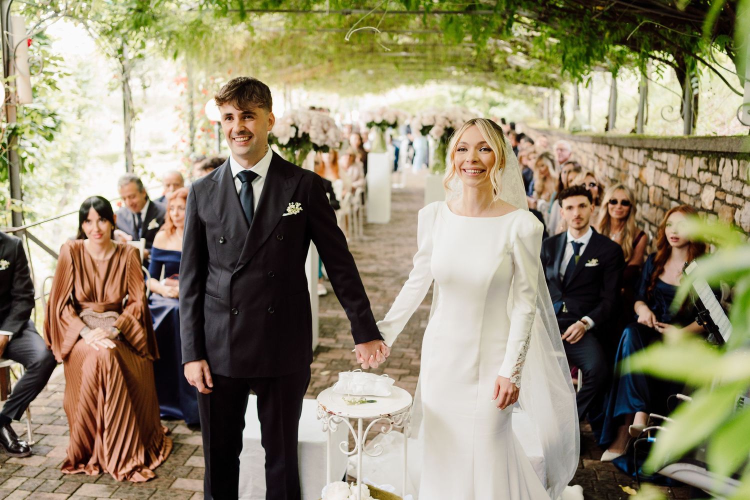 Bride and groom share a romantic moment in a vineyard, bride holding white peony bouquet in elegant long-sleeve gown.