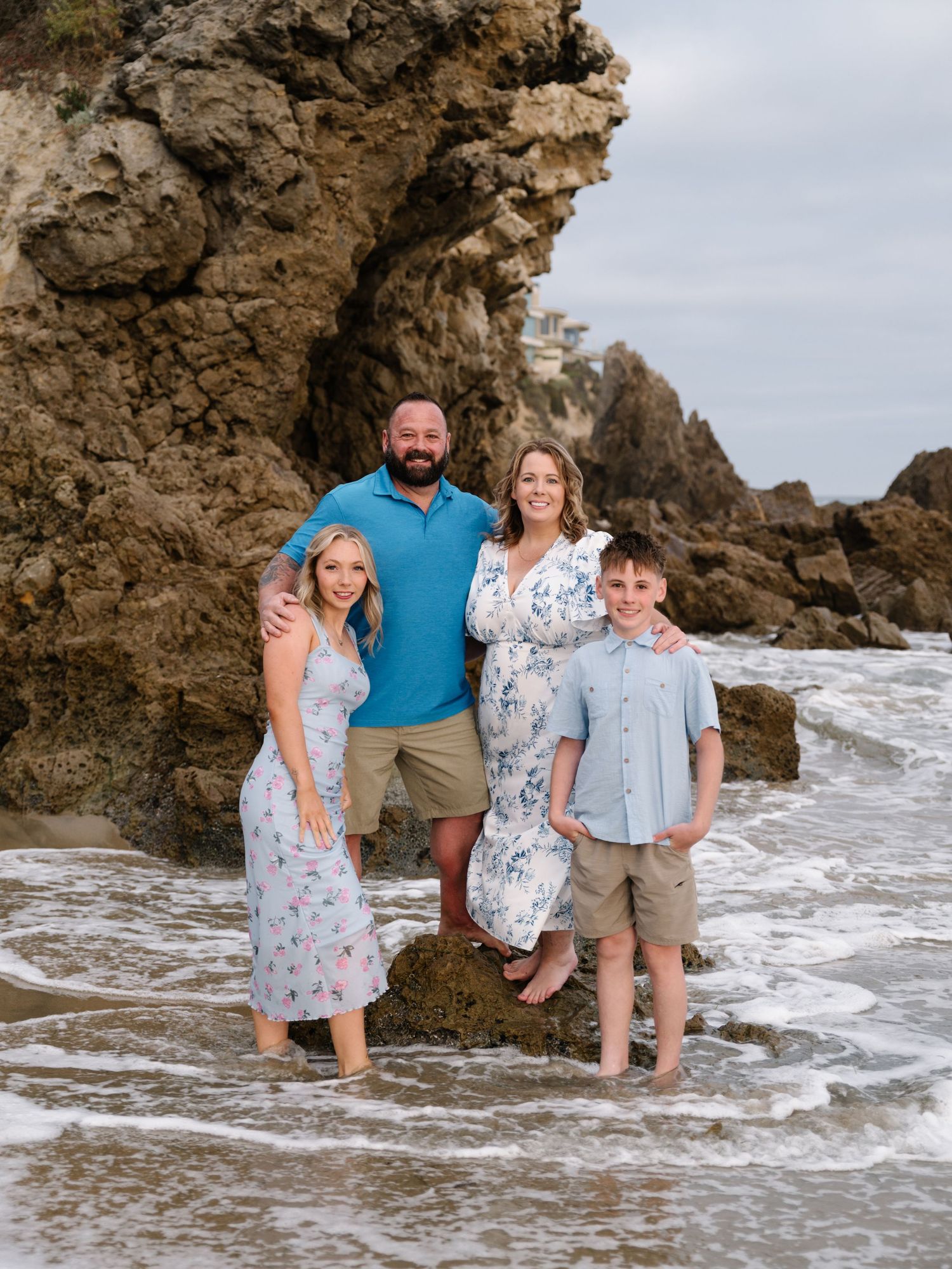 Family gathered together beside a coastal rock formation during an Orange County beach family photography session.