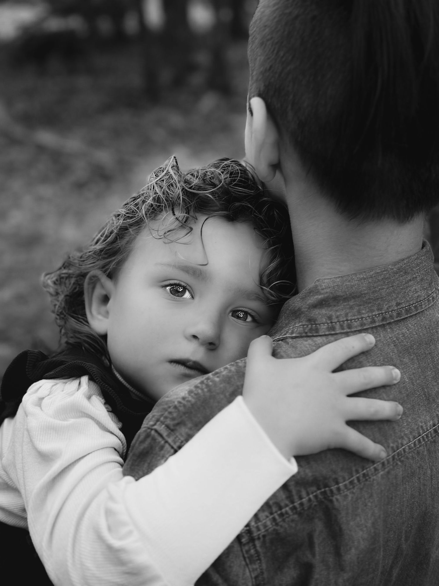 Black and white portrait of a young curly-haired child resting head on a siblings shoulder.