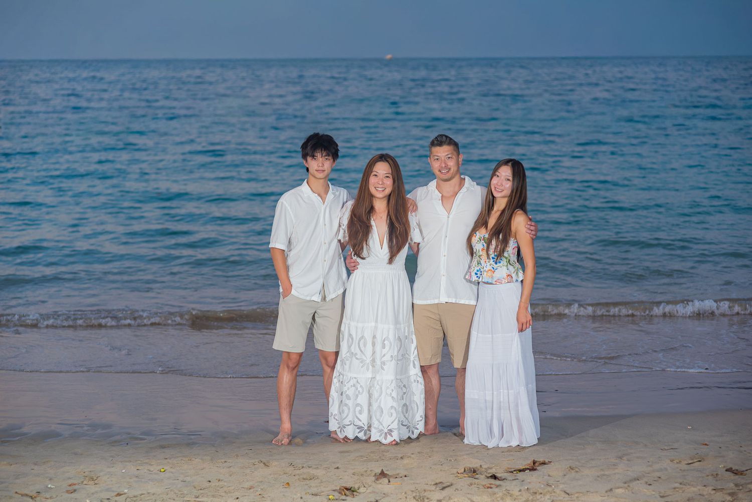 Four people posing together on a sandy beach at dusk with calm ocean waves in the background.