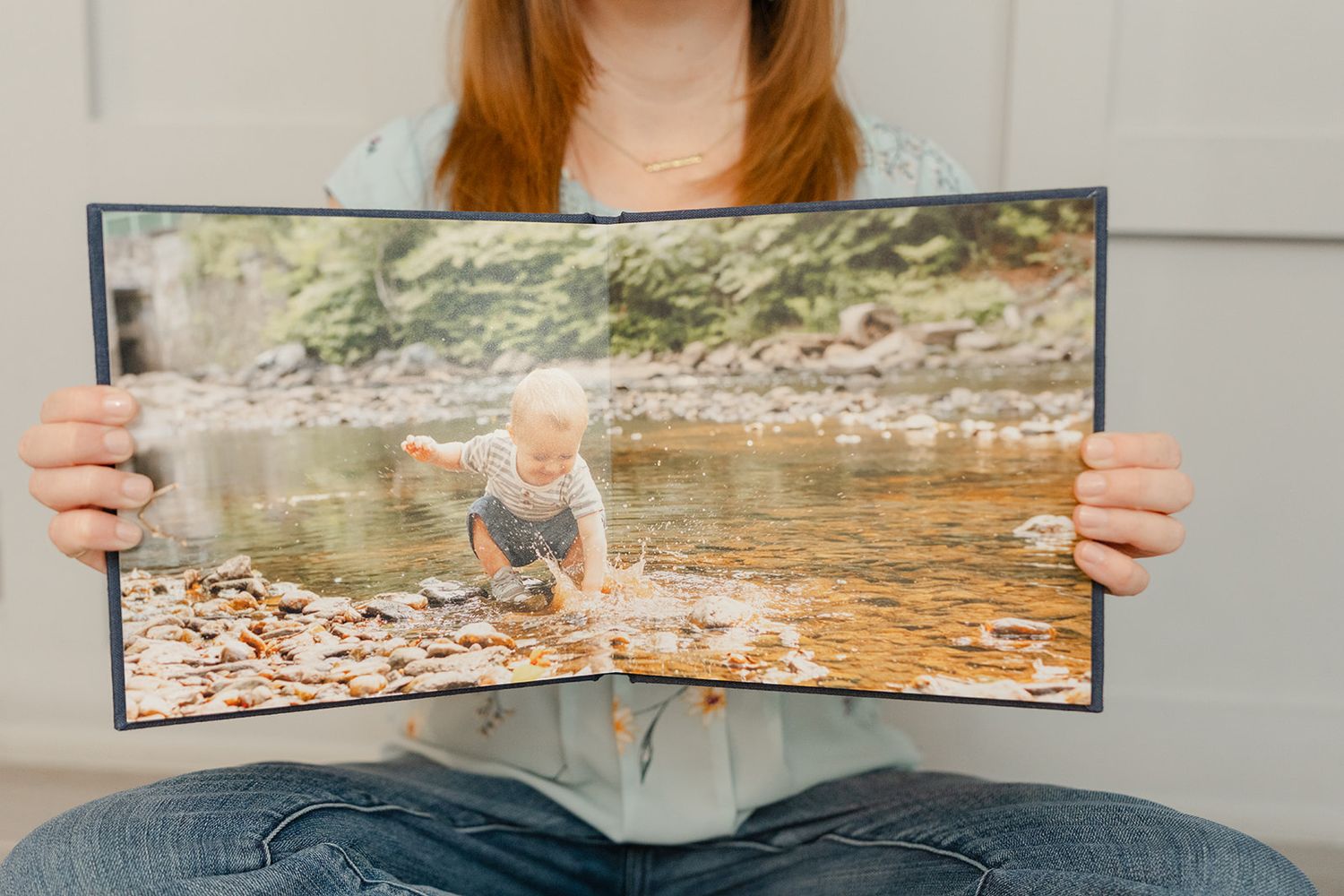 printed photo album open to an image of a boy splashing in a creek, displayed by a fall family photographer in the DC area